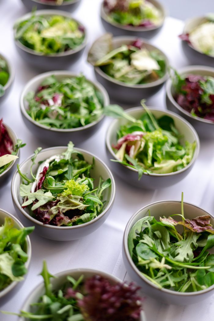 An array of mixed green salads with vibrant lettuce and arugula in ceramic bowls on a white tablecloth.